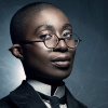 senmut: A black woman with short-cropped hair, glasses, and tie looking smug at the viewer (Sandman: Lucienne)