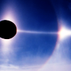 parhelicon: a parhelic circle. the sun appears eclipsed, with a corona around it, and a luminous ring that has a sundog reflection near the edge of the icon. the sky is intense blue. (Default)